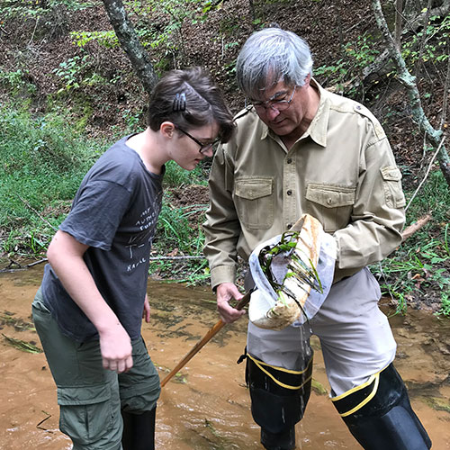 Photo of student and teacher in the field examing samples taken from water