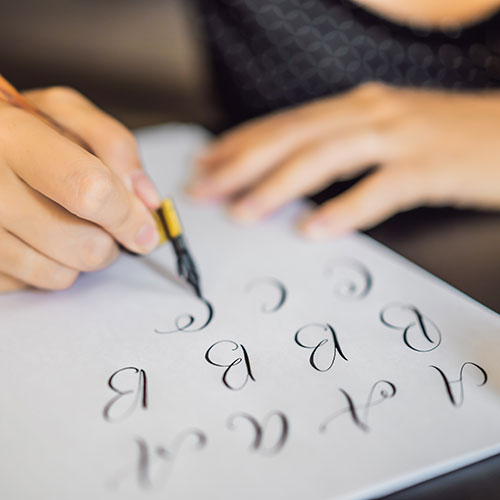 Hands shown creating letters with metal nibbed pen.