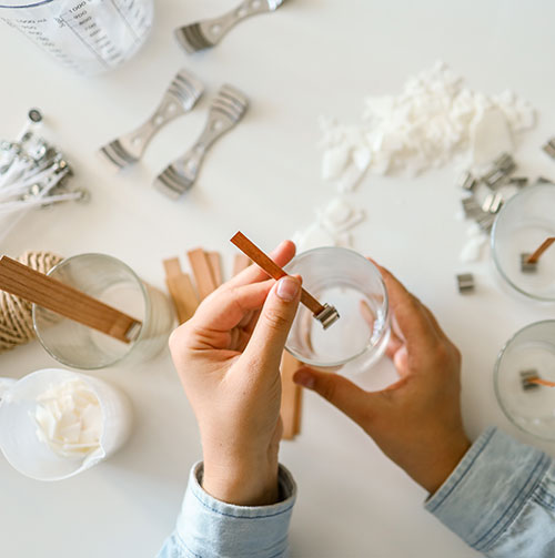 hands shown setting a wick into a candle container with other supplies in background