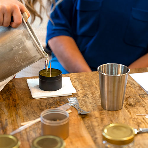 student in background with candle making items on table