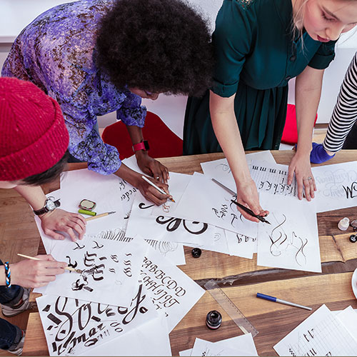 Students working at table using brushes and pens to create lettering
