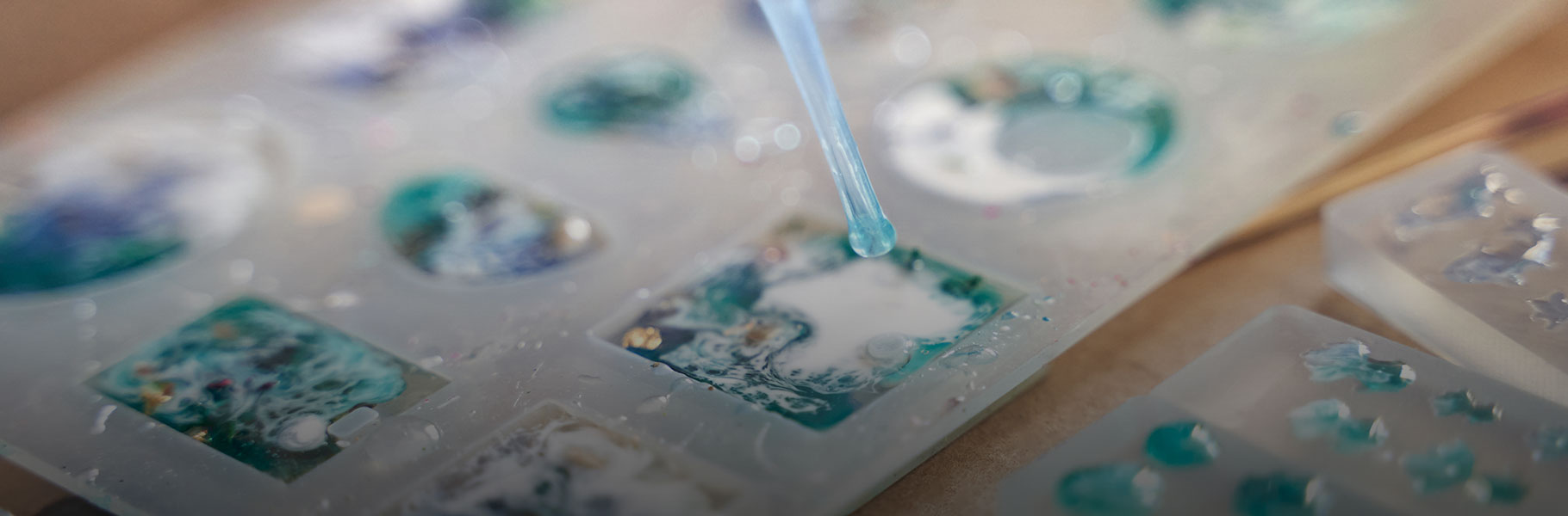 Close up of resin art process with colorful designs and pipette application on molded shapes.