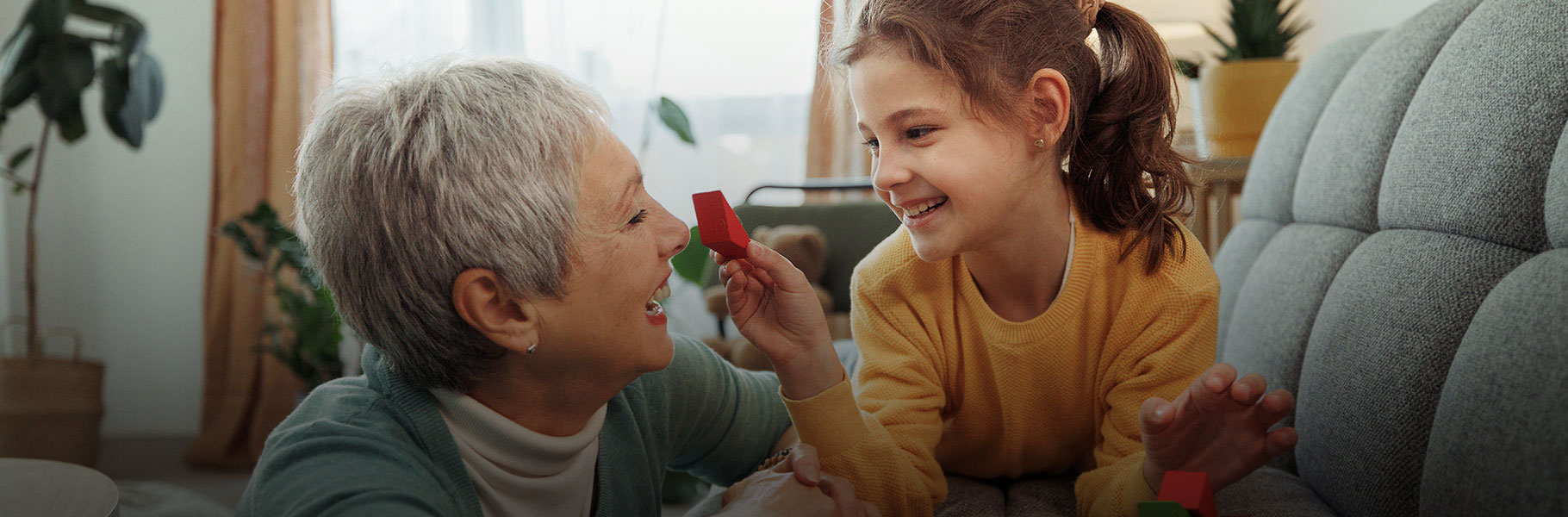 Grandmother and granddaughter enjoy playful moments together, building with wooden toy blocks in their home