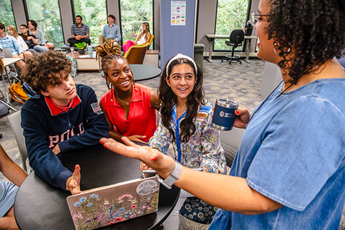 three students having a discussion with professor in college classroom