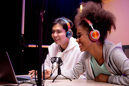 two students with headphones on speaking into recording microhpone