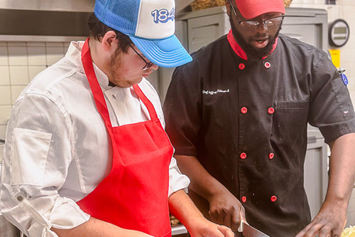 three students in test kitchen wearing red aprons
