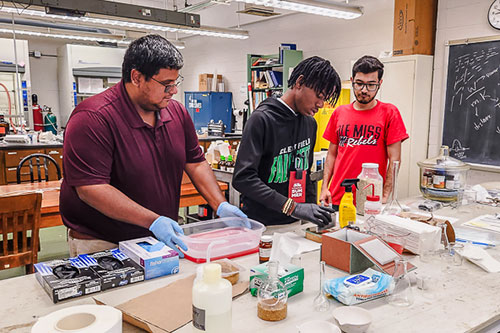three students working on experiment in classroom during program