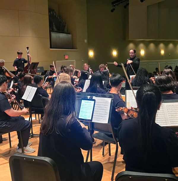 students in symphony playing various instruments with conductor