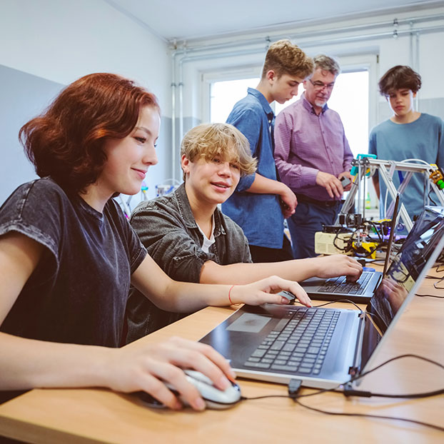two students looking at data on a laptop while two students and an instructor in background look at 3-d project