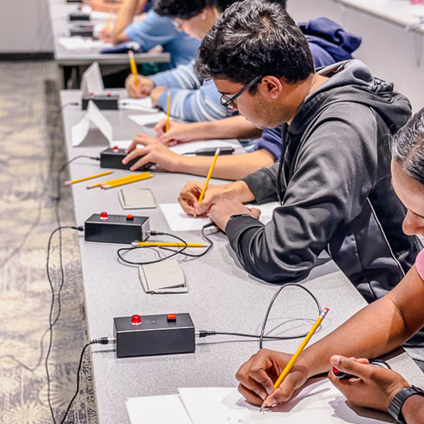 students in classroom with quiz buzzers making notes on paper
