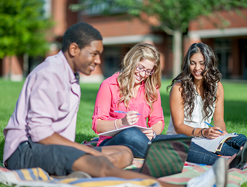 three students outdoors on campus writing in notebooks