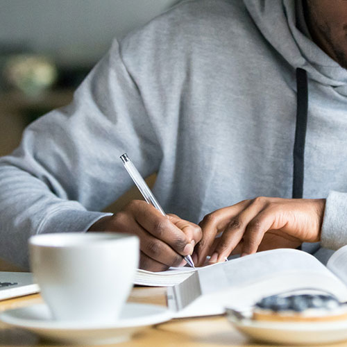 Student writing in notebook with coffee on table