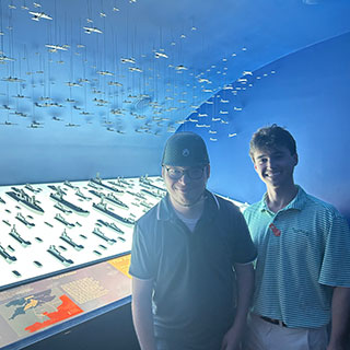 students posing in front of display of plane and submarine models in WW2 museum