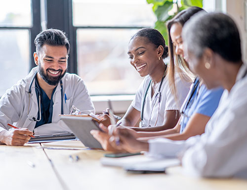 A small group of four medical professionals sit around a boardroom table as they meet to discuss patient cases.