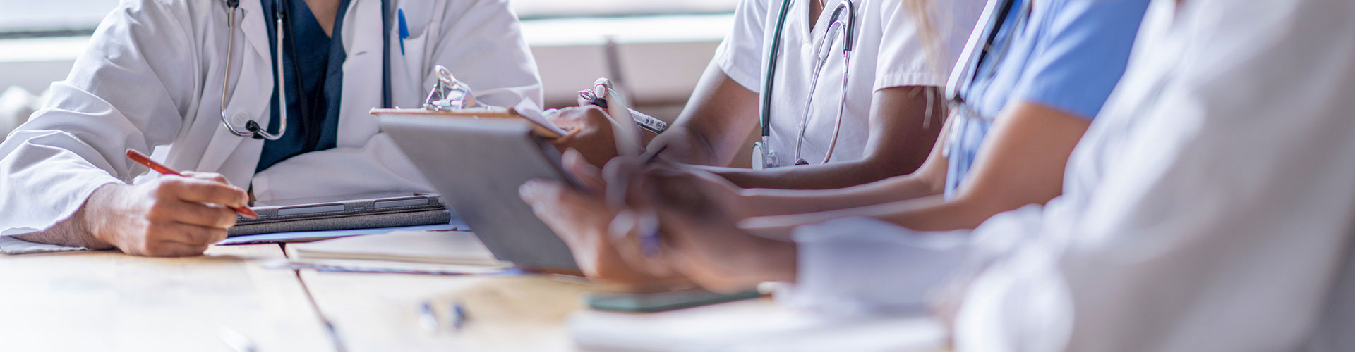 A small group of four medical professionals sit around a boardroom table as they meet to discuss patient cases.